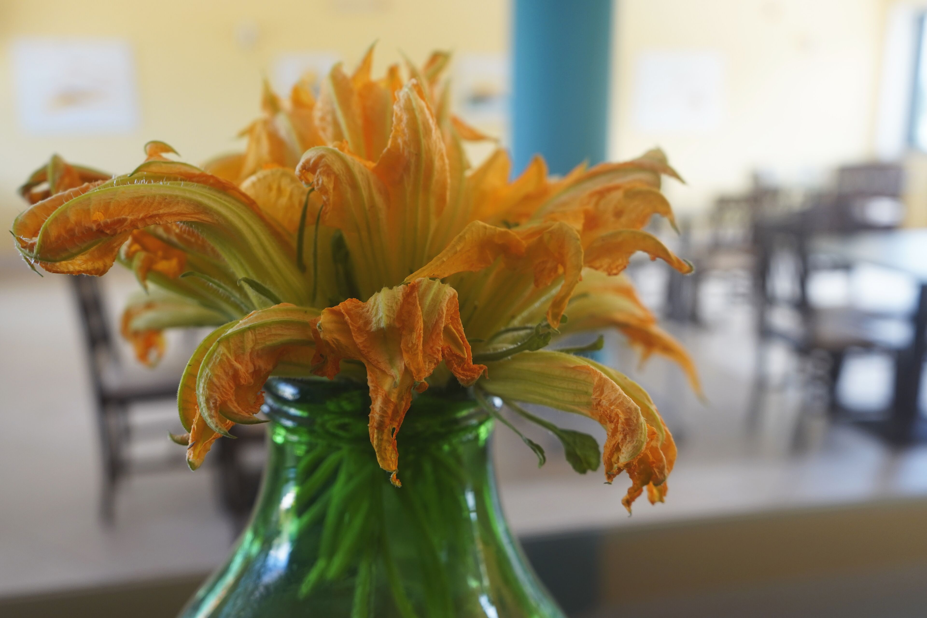 Eine grüne Vase mit welken, orangefarbenen Blüten.