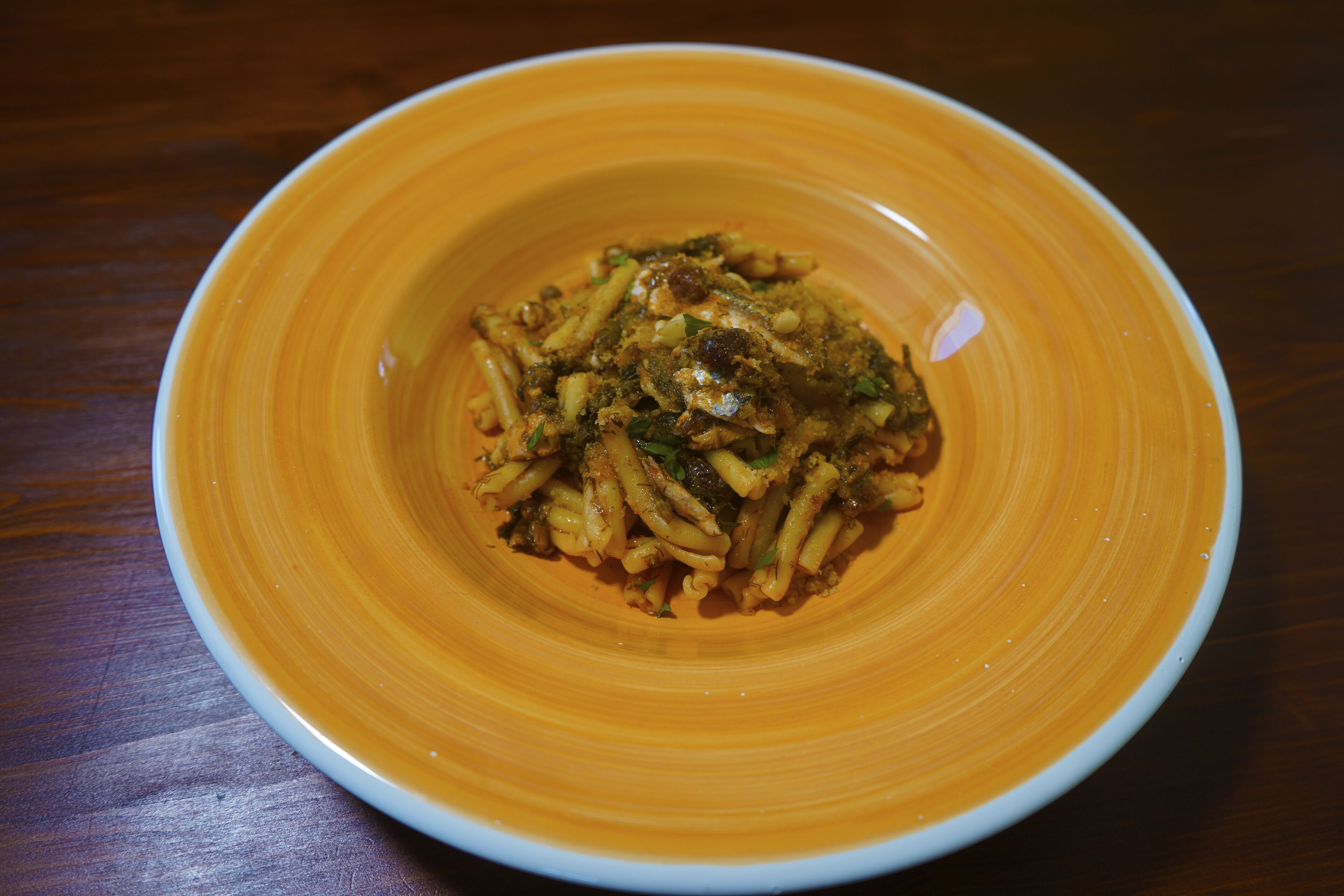 Een kom pasta met saus op een houten tafel.