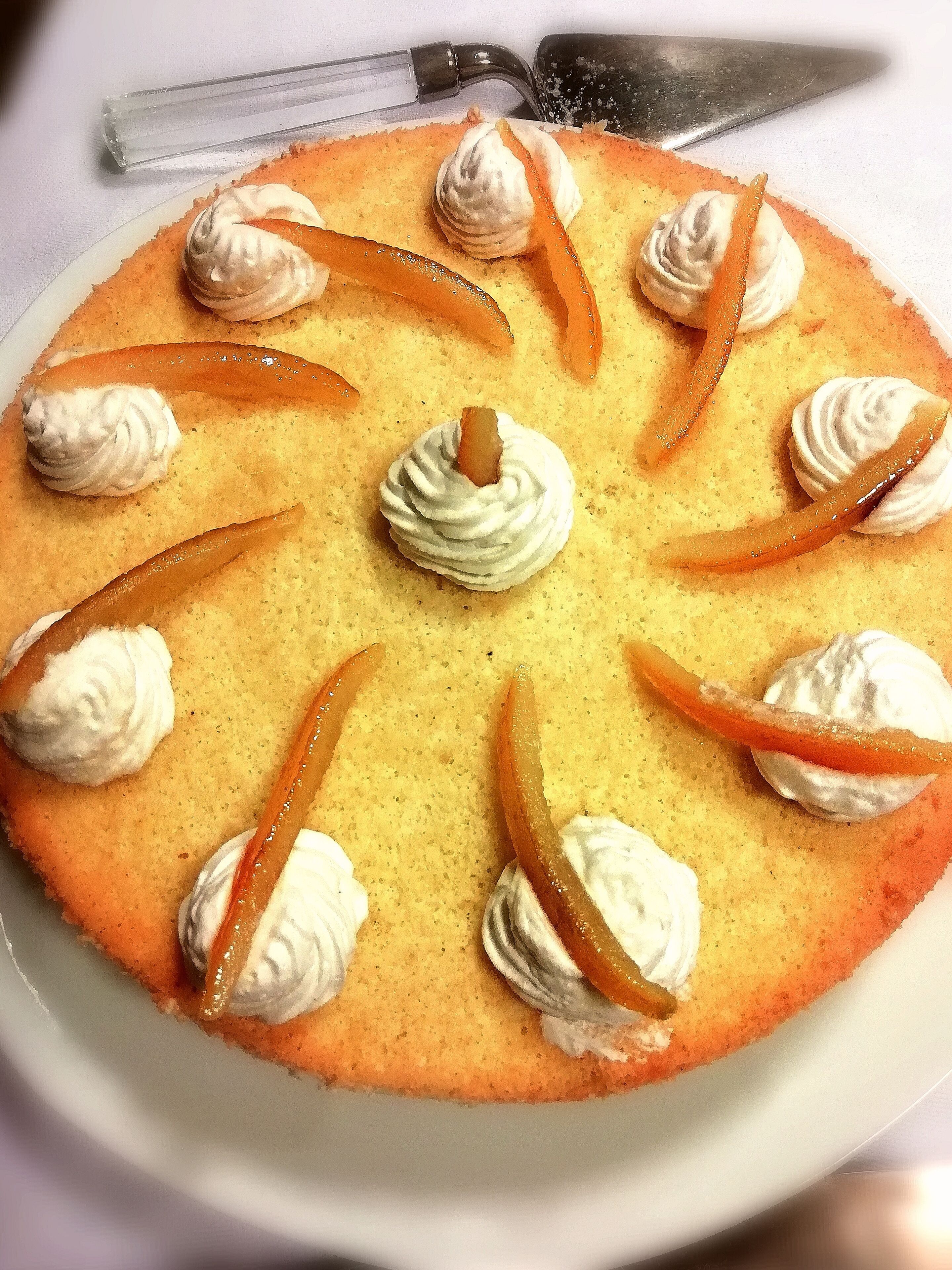 Ein runder Kuchen mit Schlagsahne und Orangenscheiben auf einem weißen Teller.