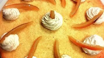 Ein runder Kuchen mit Schlagsahne und Orangenscheiben auf einem weißen Teller.