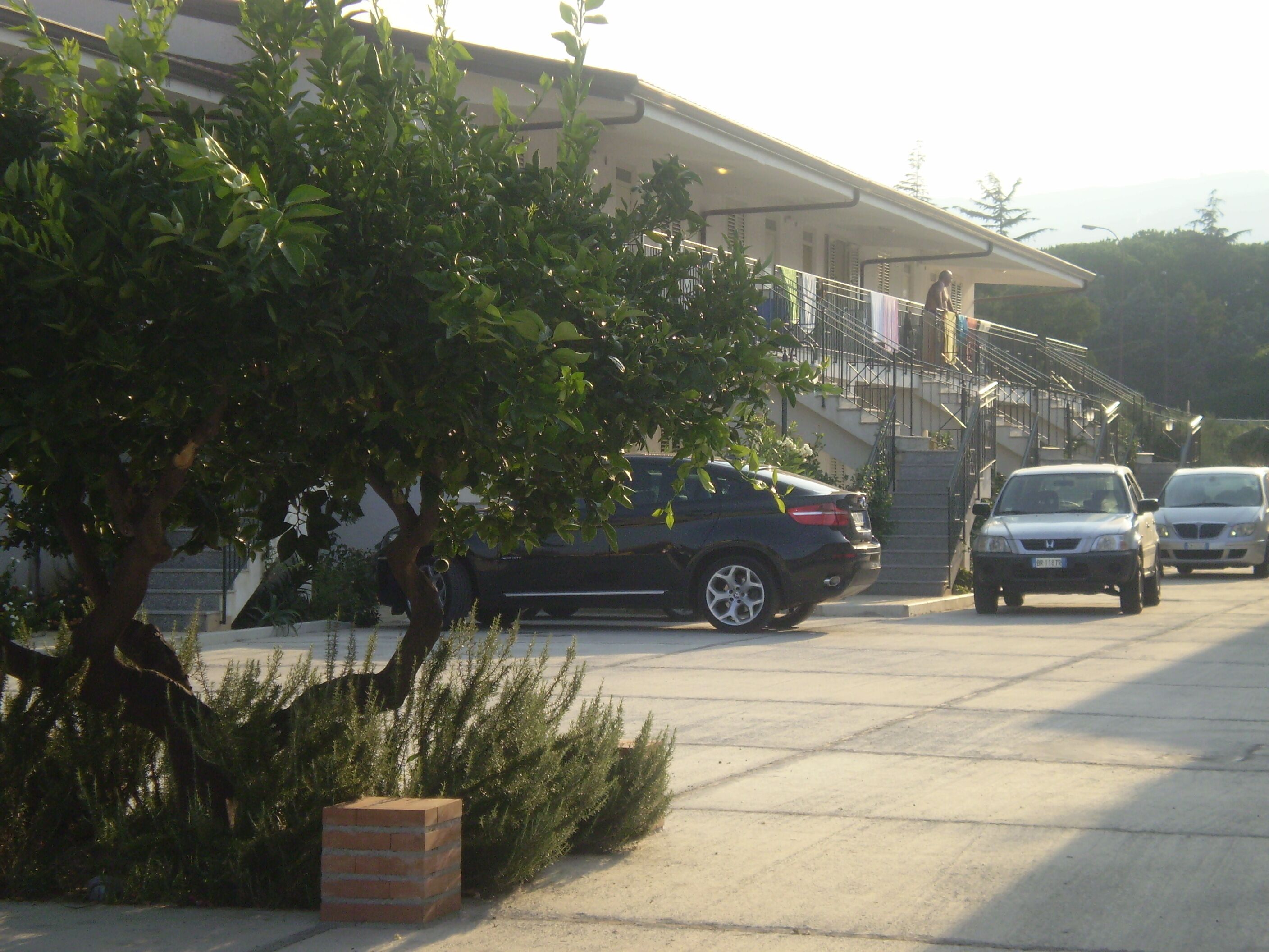A parking area with cars, a building with a staircase, and a tree.