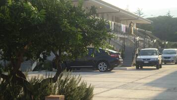 A parking area with cars, a building with a staircase, and a tree.