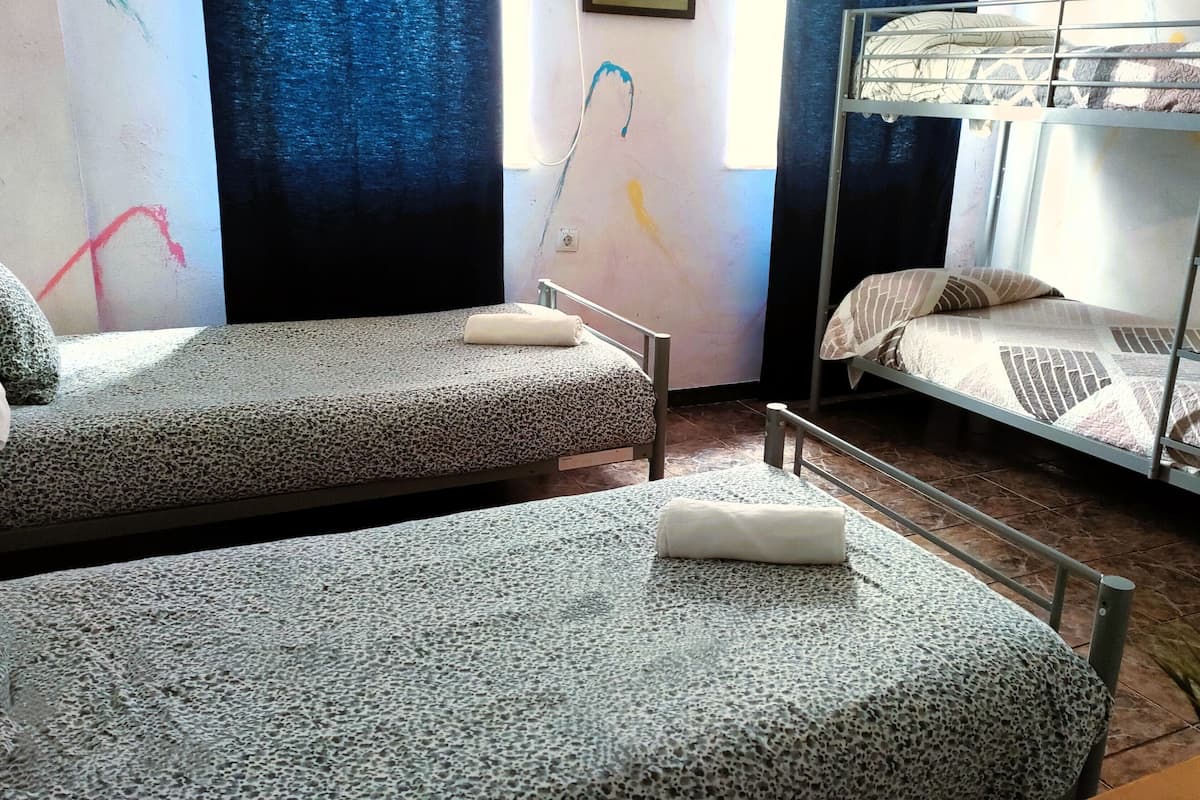 A dormitory room with two single beds, a bunk bed, and a small potted plant.