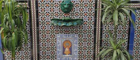 Una fuente de azulejos con diseños geométricos y una estatua en el centro, rodeada de plantas en macetas.