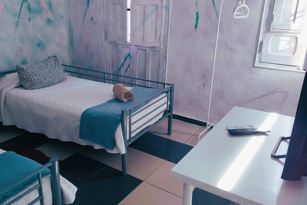 A bedroom with a bed, a bedside table, a desk, and a chair.