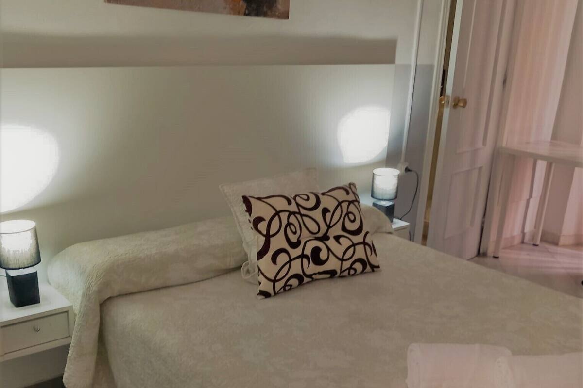 A neatly made bed with a patterned pillow, two bedside lamps, and a painting above the bed.