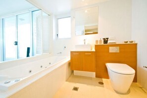 A modern bathroom with a large bathtub, wooden vanity, and a toilet.