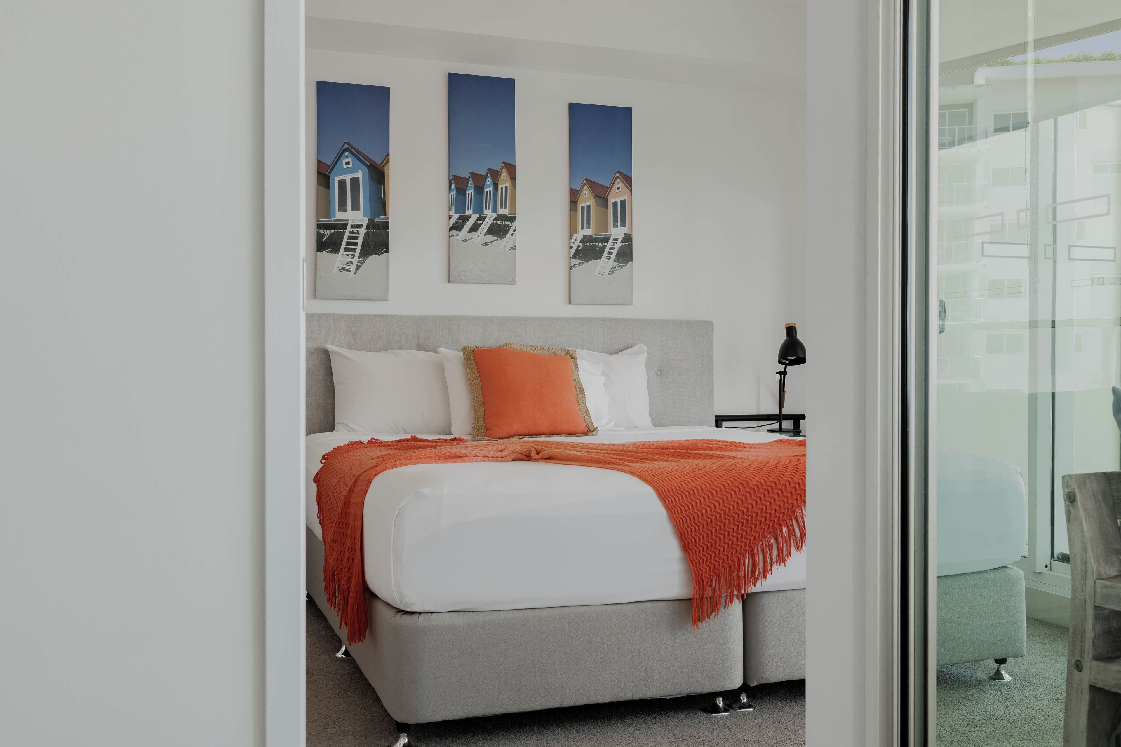 A modern bedroom with a bed, a nightstand, and a window with a view of buildings.