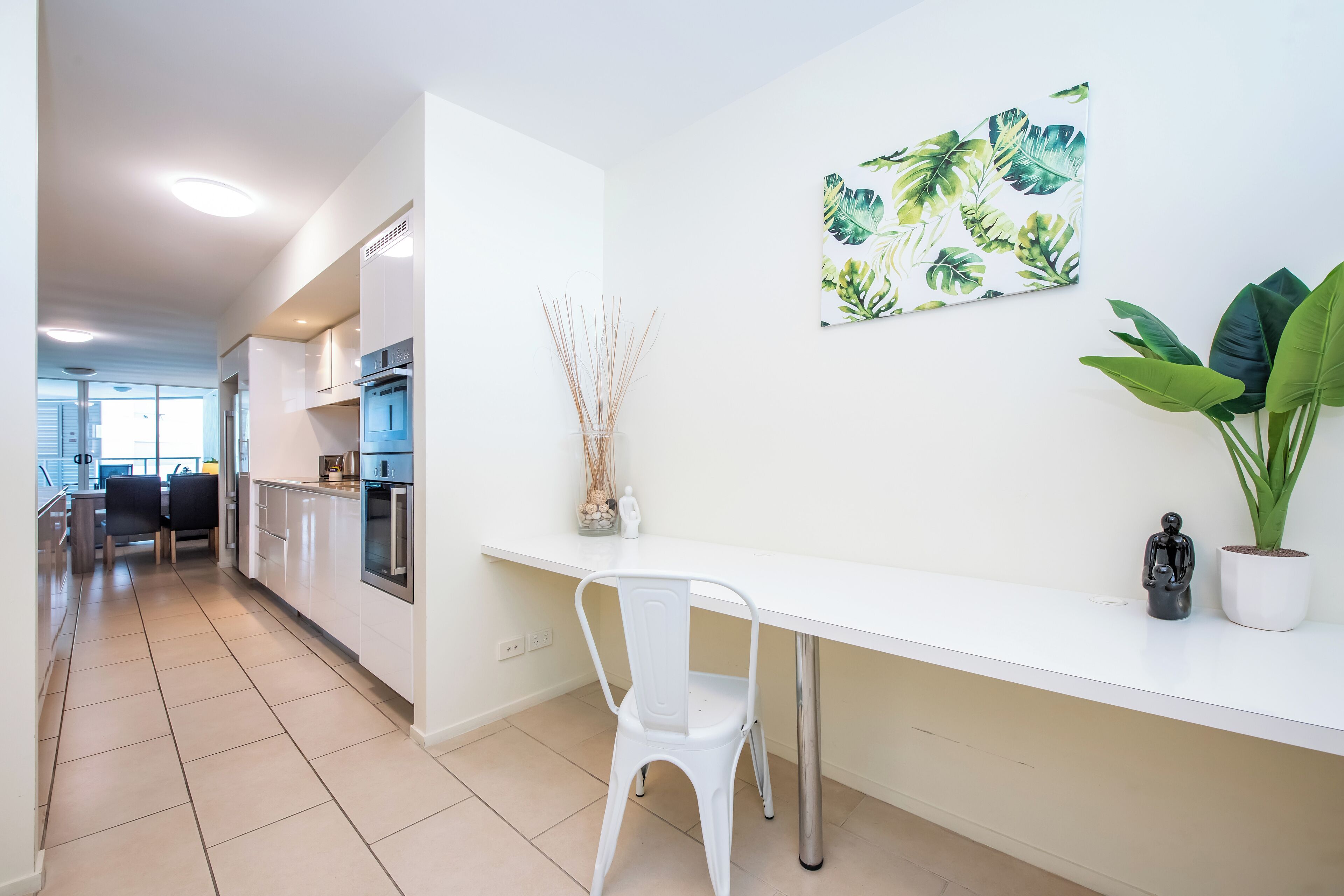 Une cuisine moderne avec des meubles blancs, un plan de travail blanc et un coin repas agrémenté d’une chaise blanche.