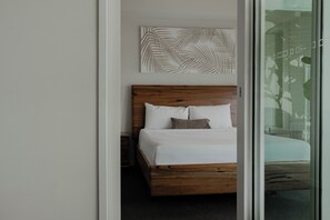 A modern bedroom with a wooden bed frame, white bedding, and a large window with a view of greenery.