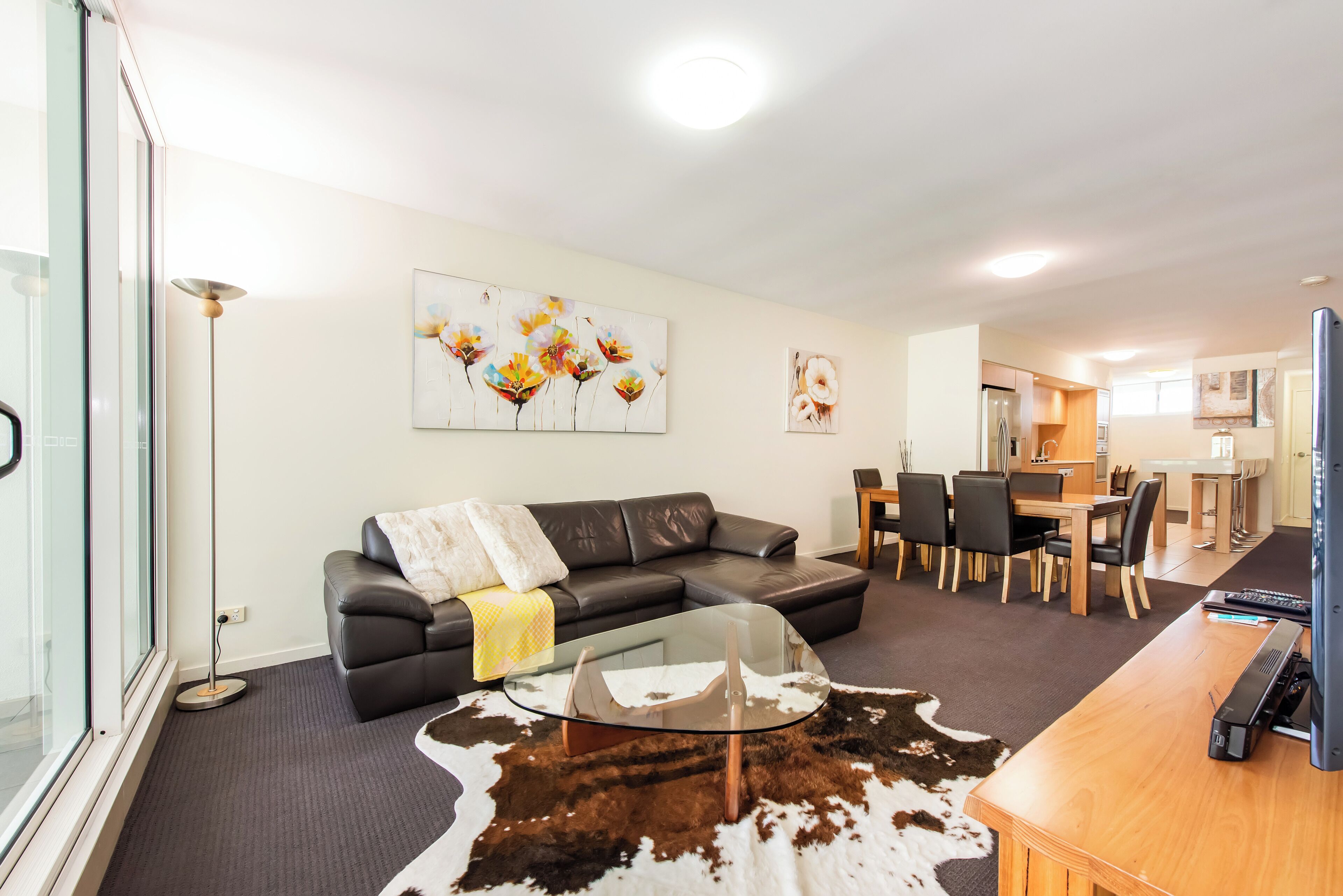 A modern living room with a glass coffee table, a leather sofa, and a dining area with a wooden table and chairs.