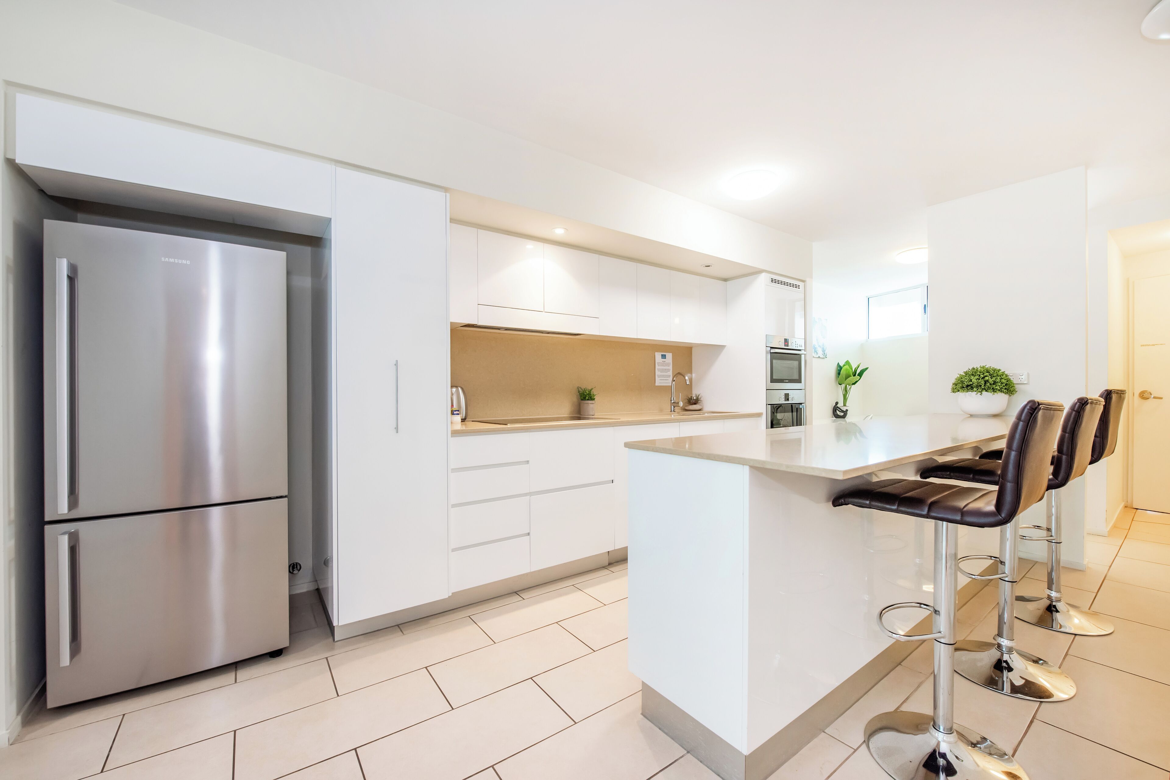 Een moderne keuken met een roestvrijstalen koelkast, witte kasten, een centraal eiland met barstoelen en een klein aanrecht.