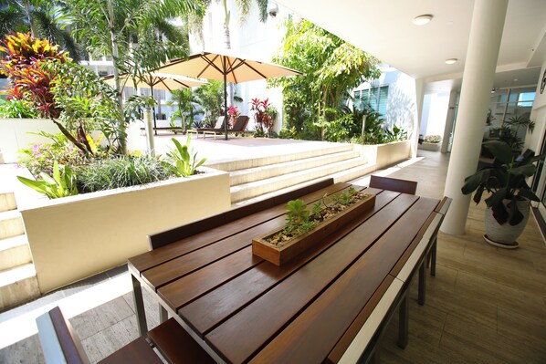 A wooden bench with a planter box, surrounded by lush greenery and a large umbrella.