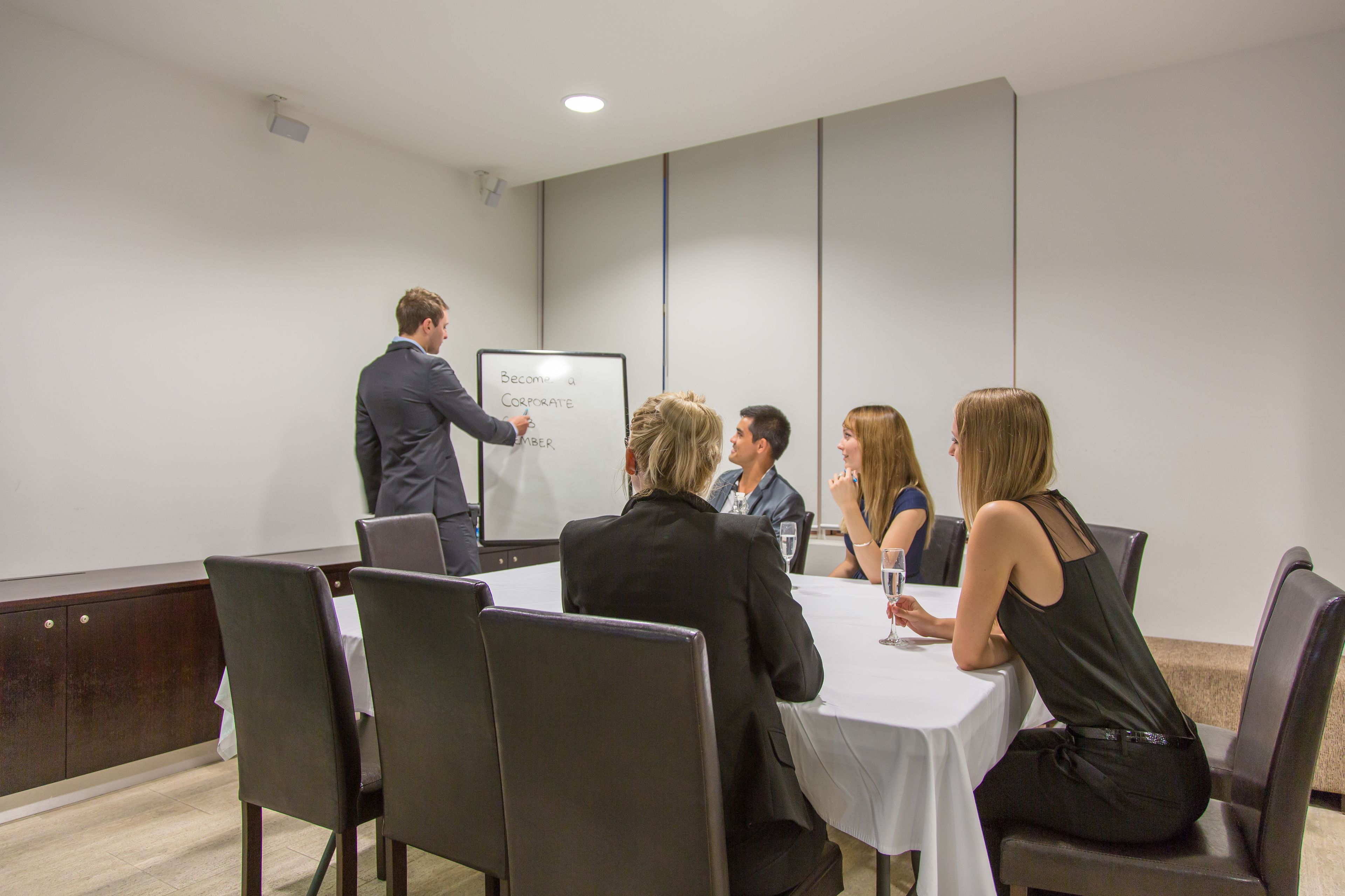 Une salle de conférence équipée d’un tableau blanc, avec un présentateur et des participants assis autour d’une table.