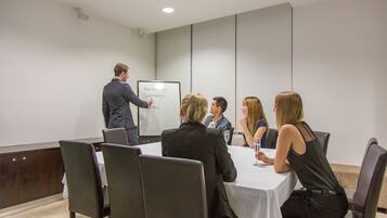 Une salle de conférence équipée d’un tableau blanc, avec un présentateur et des participants assis autour d’une table.