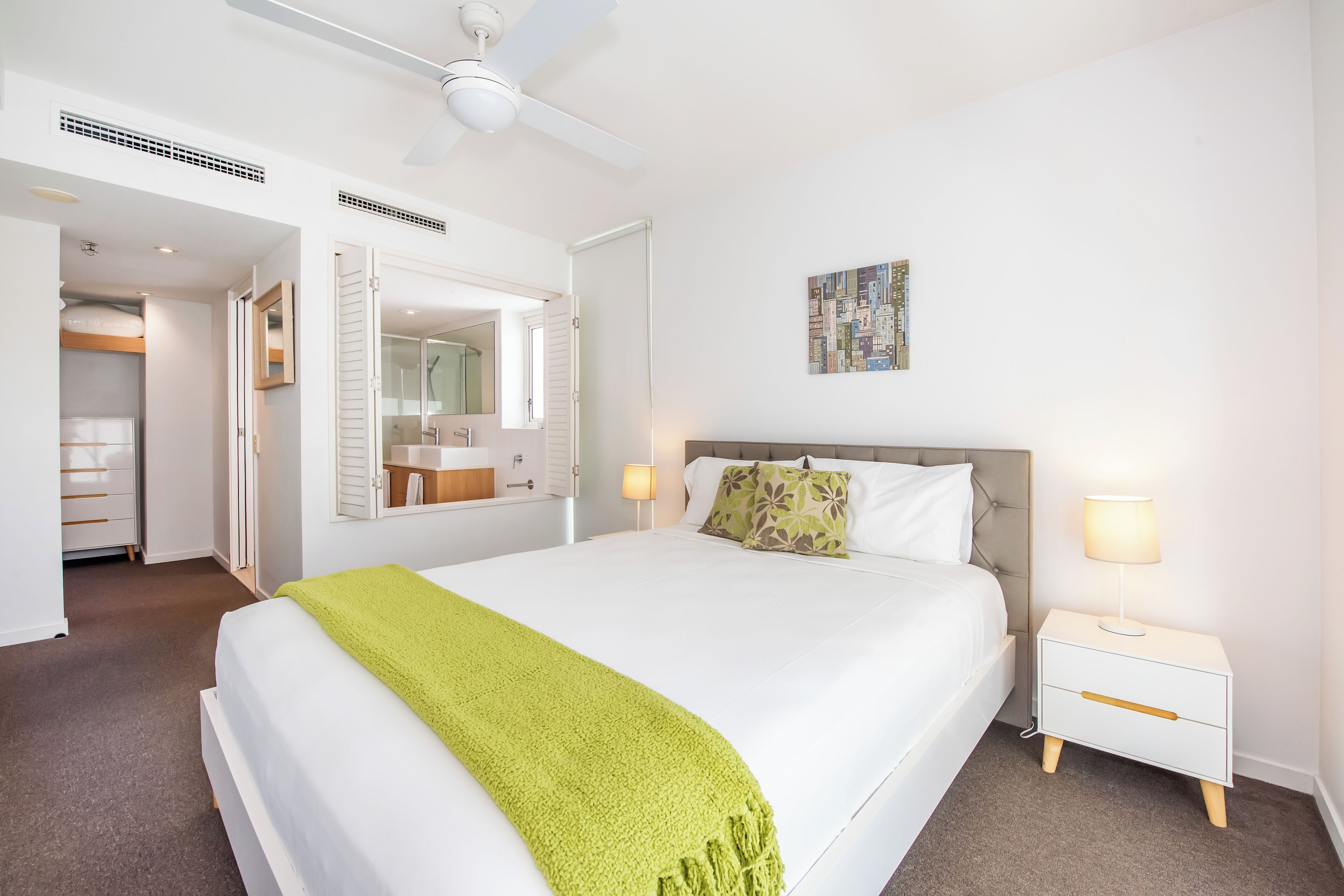 A bedroom with a bed, bedside table, lamp, and a painting on the wall.