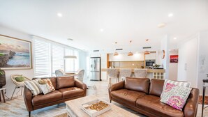 A modern living room with brown leather sofas, a wooden coffee table, and a kitchen in the background.