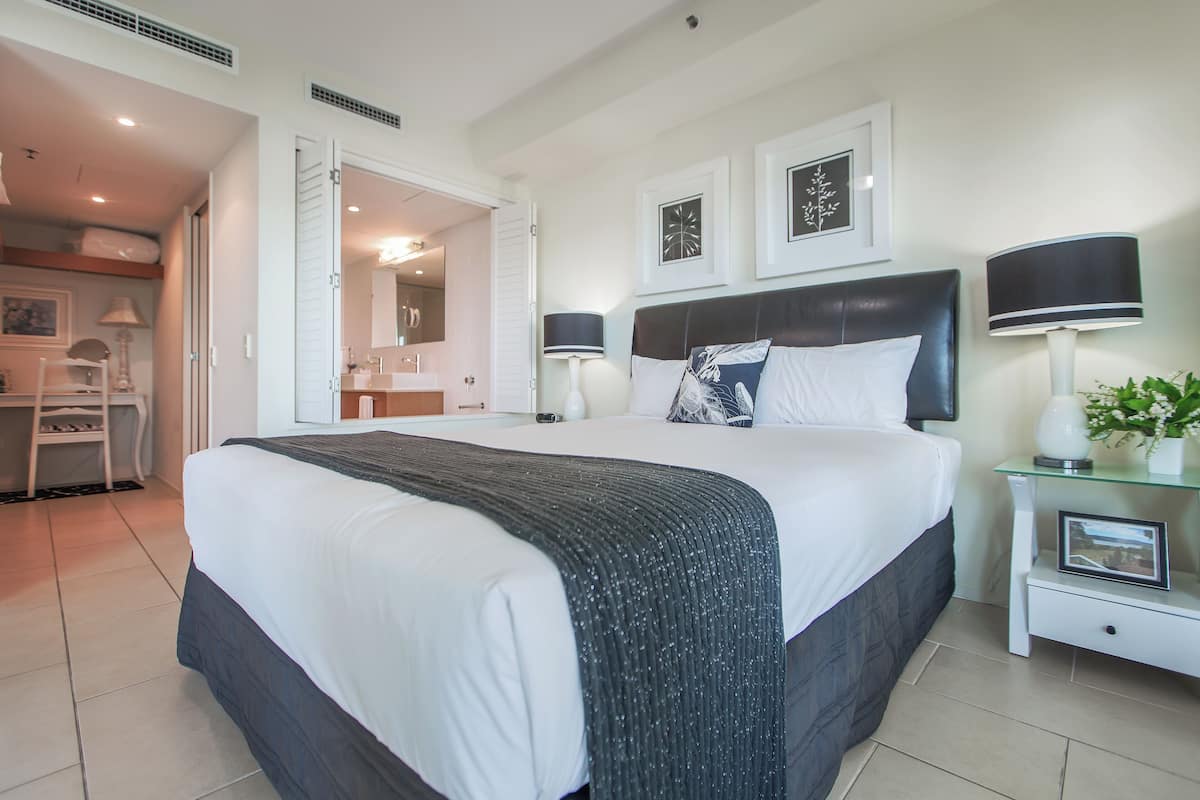 A modern hotel room with a large bed, bedside lamps, a glass side table, and framed artwork on the wall.