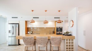 A modern kitchen with a central island, stainless steel appliances, and three wicker bar stools.