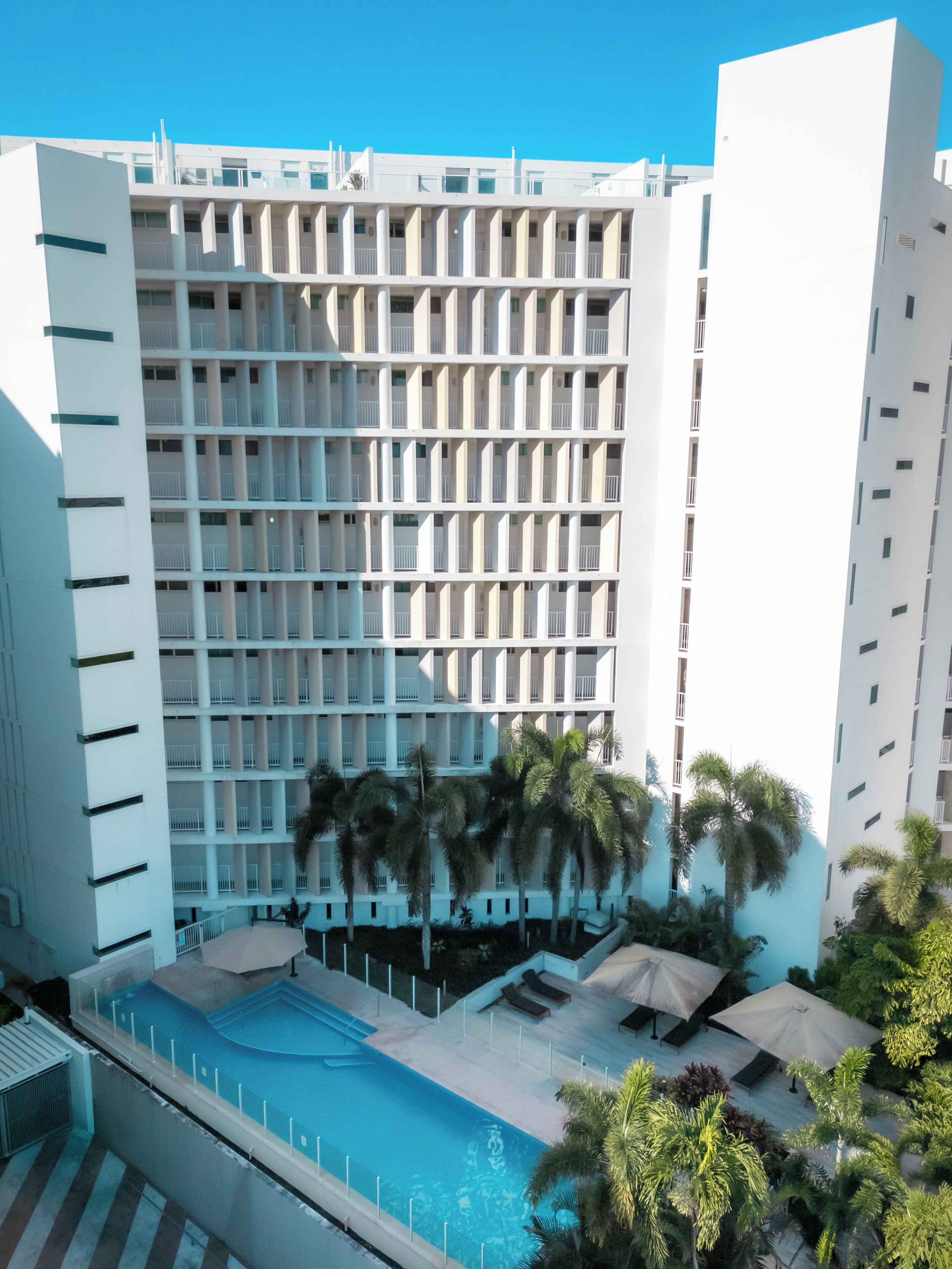 Ein modernes Hotel mit Poolbereich, mehreren Balkonen und Palmen.