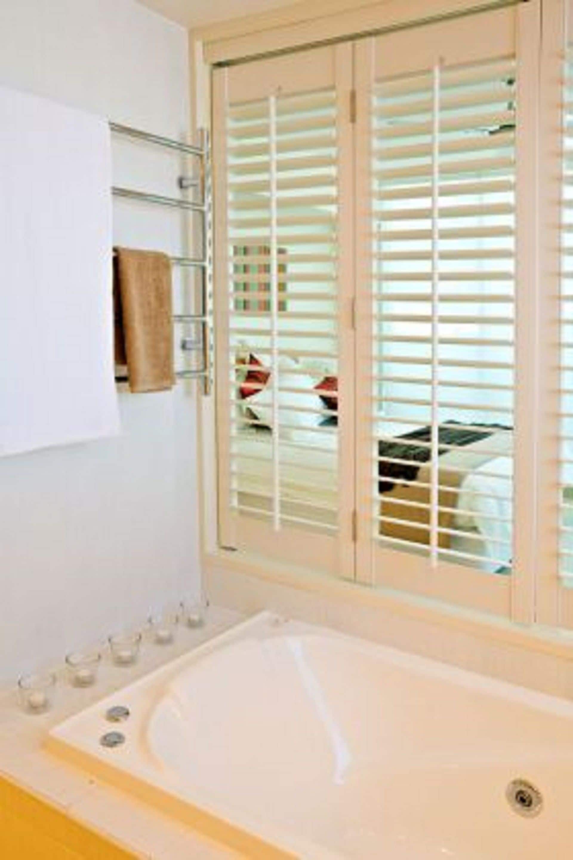 Un baño con bañera, toallero y ventana con persianas.