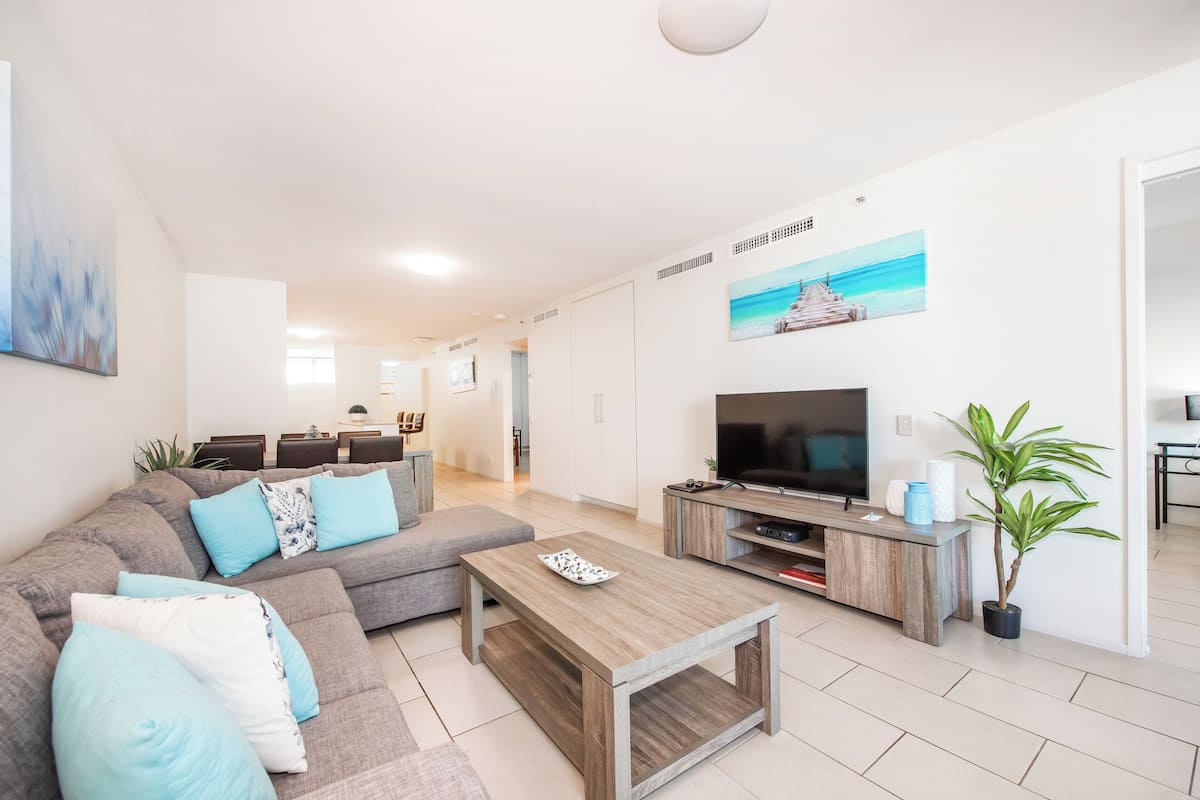 A modern living room with a sectional sofa, a coffee table, a TV, and a potted plant.