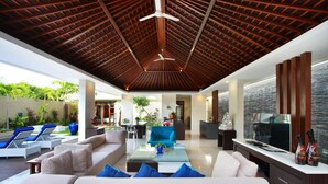 A spacious living area with a wooden ceiling, a sofa set, a coffee table, and a TV. - Indi Villas - The Ambika (Seminyak)
