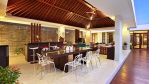 A modern indoor space with a central dining area, white chairs, and a wooden ceiling. - Indi Villas - The Ambika (Seminyak)