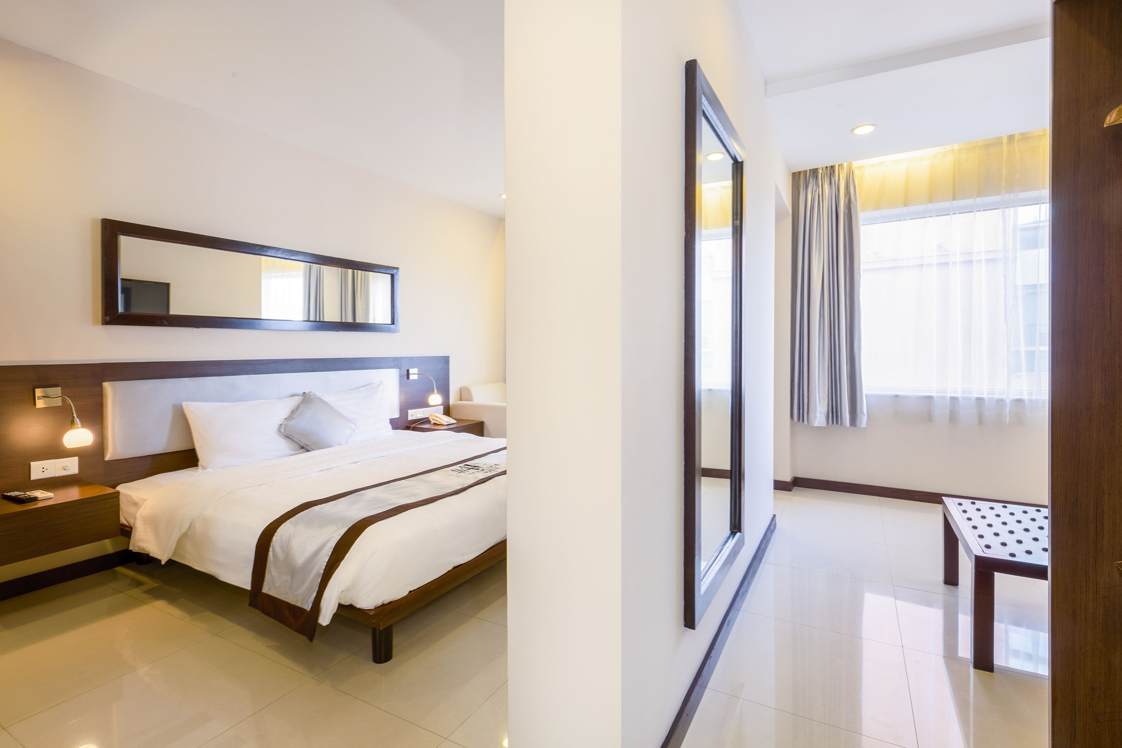 Une chambre d’hôtel avec un lit, une table de chevet, une lampe et un grand miroir au mur.
