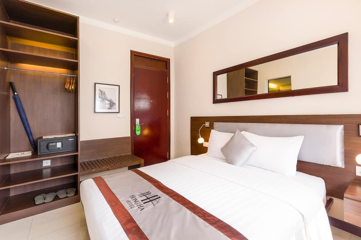 A hotel room with a bed, a wardrobe, a mirror, and a bedside table.