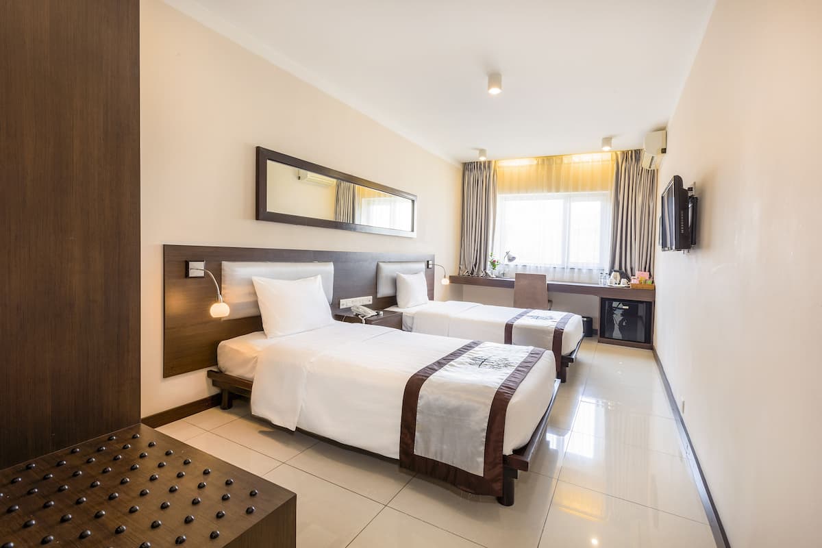 A hotel room with two beds, a desk, a TV, and a large window with curtains.