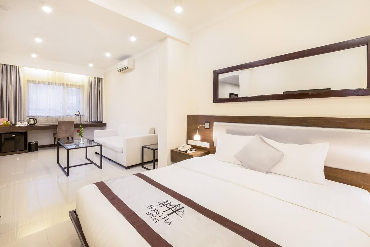 A hotel room with a large bed, a desk, a chair, and a small table.
