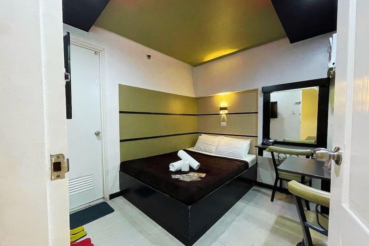 A hotel room with a bed, bedside table, and a mirror.