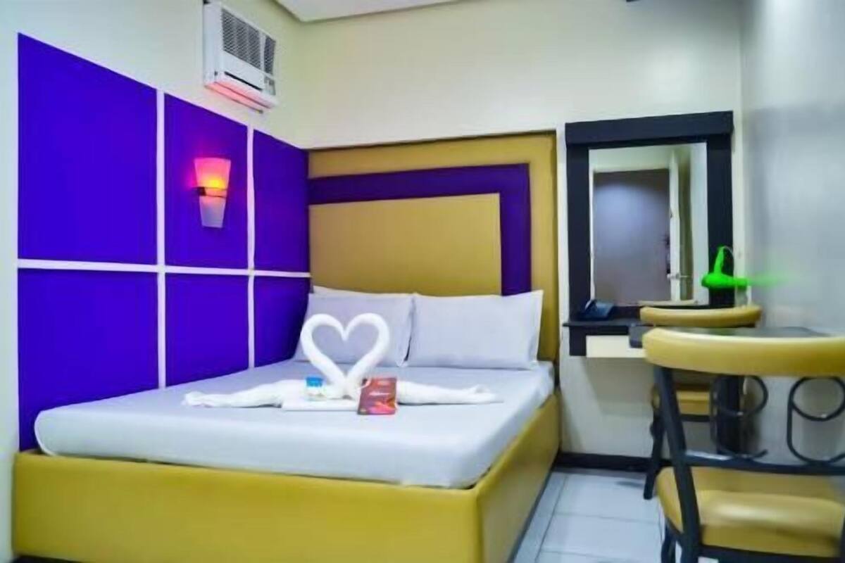 A hotel room with a bed, a bedside table, a mirror, and a wall-mounted air conditioner.