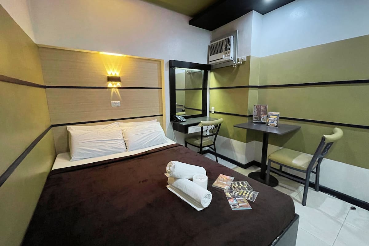 A hotel room with a bed, a desk, a chair, and a small table.