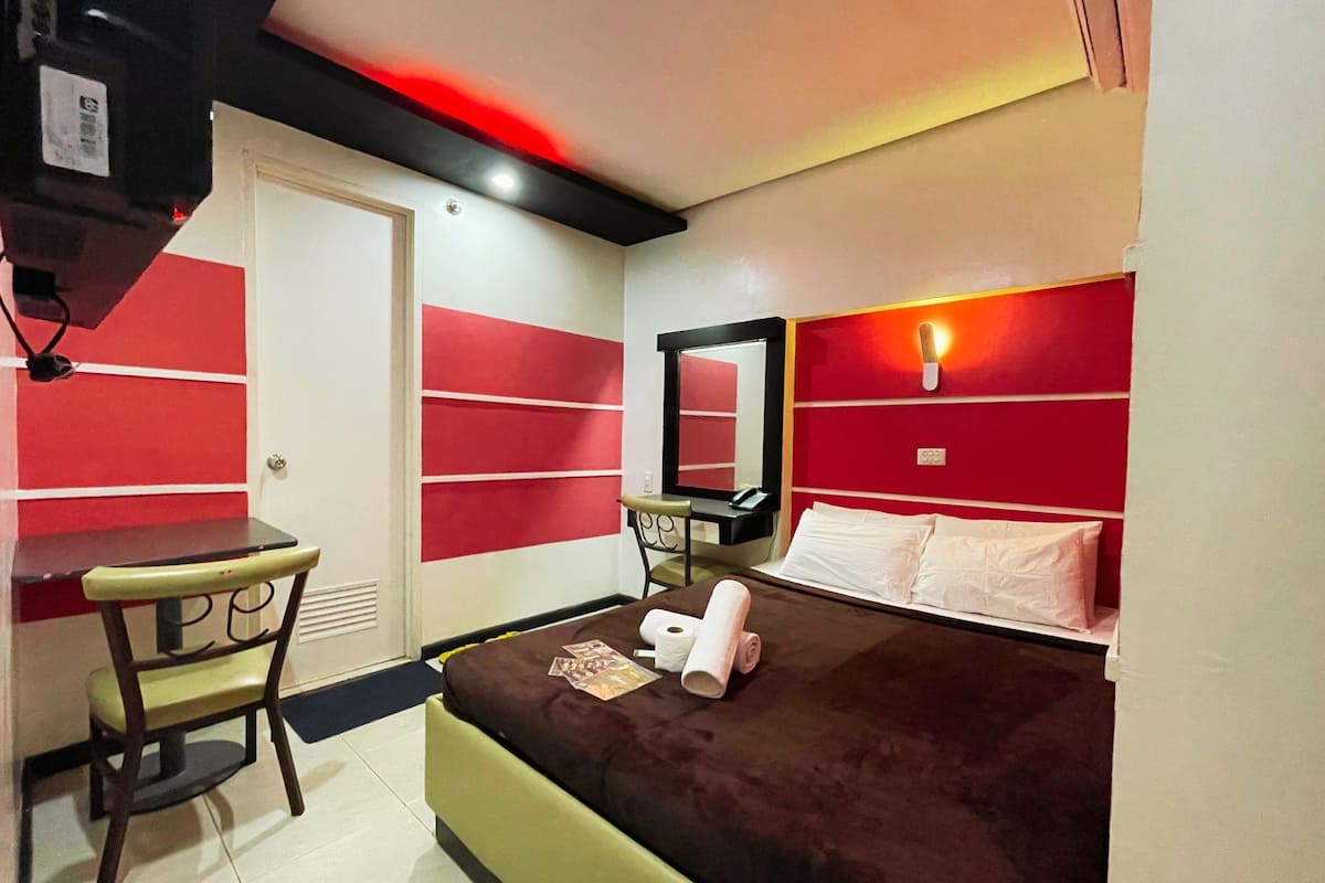 A hotel room with a bed, a desk, a chair, and a mirror.