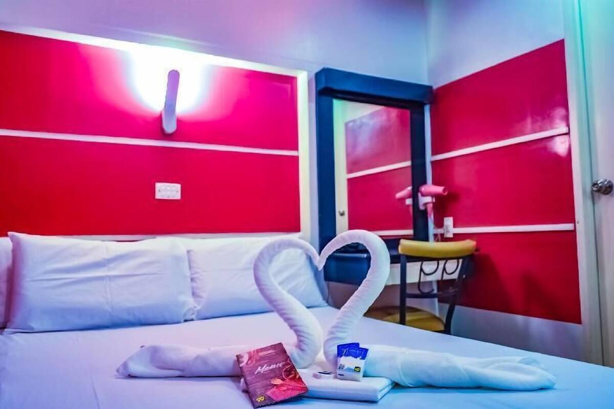 A hotel room with a bed, a heart-shaped towel, a chocolate bar, and a bottle of water.