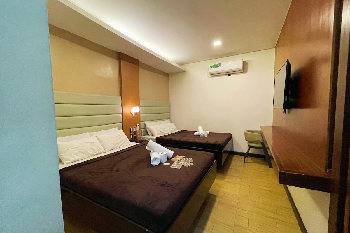 A hotel room with two beds, a TV mounted on the wall, and a wooden floor.