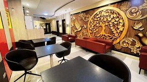 Un moderno vestíbulo de hotel con asientos negros y rojos, una pared decorativa con diseño de árbol y un piso a cuadros.