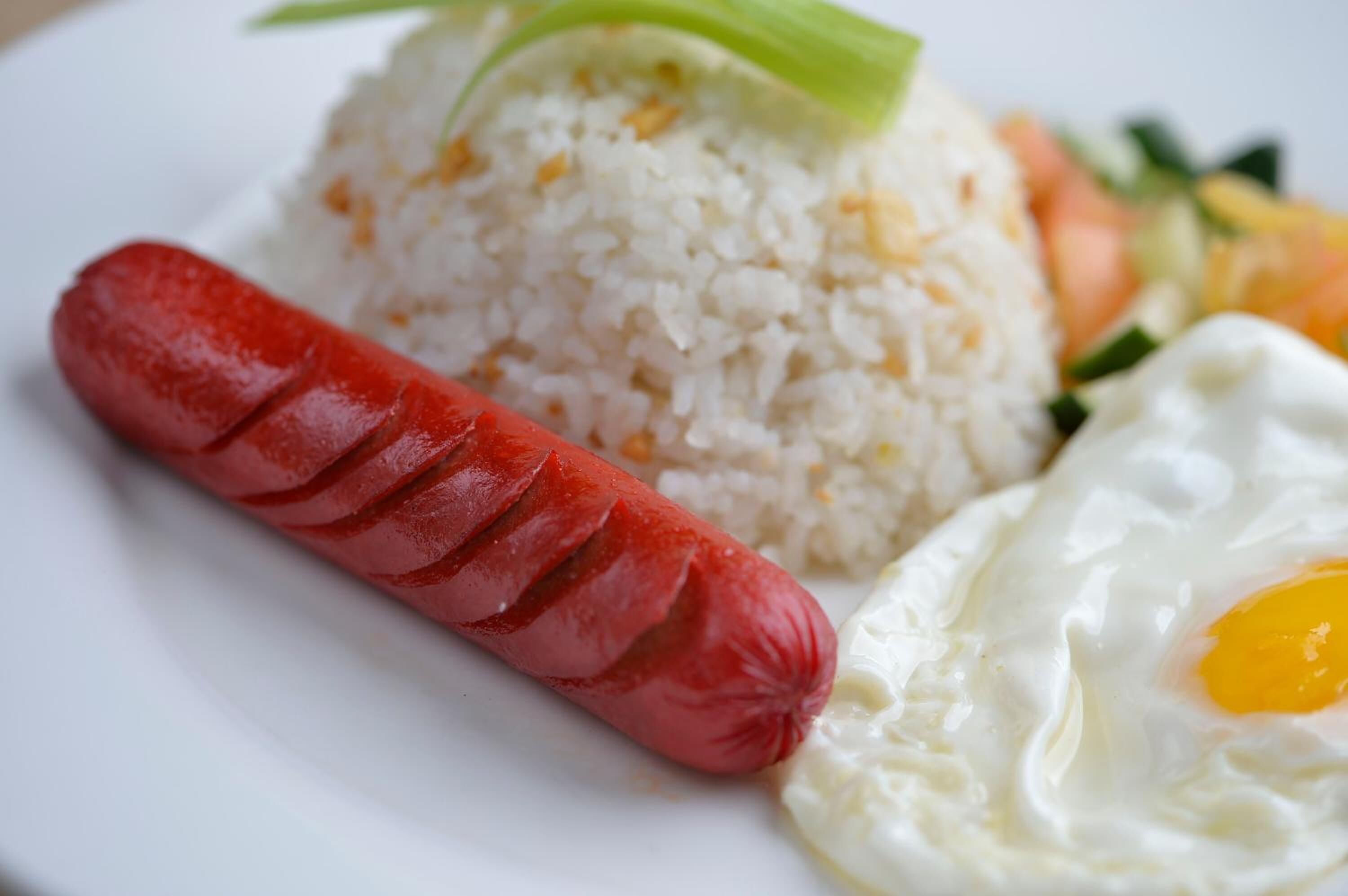 A plate with white rice, a sliced sausage, and a fried egg.