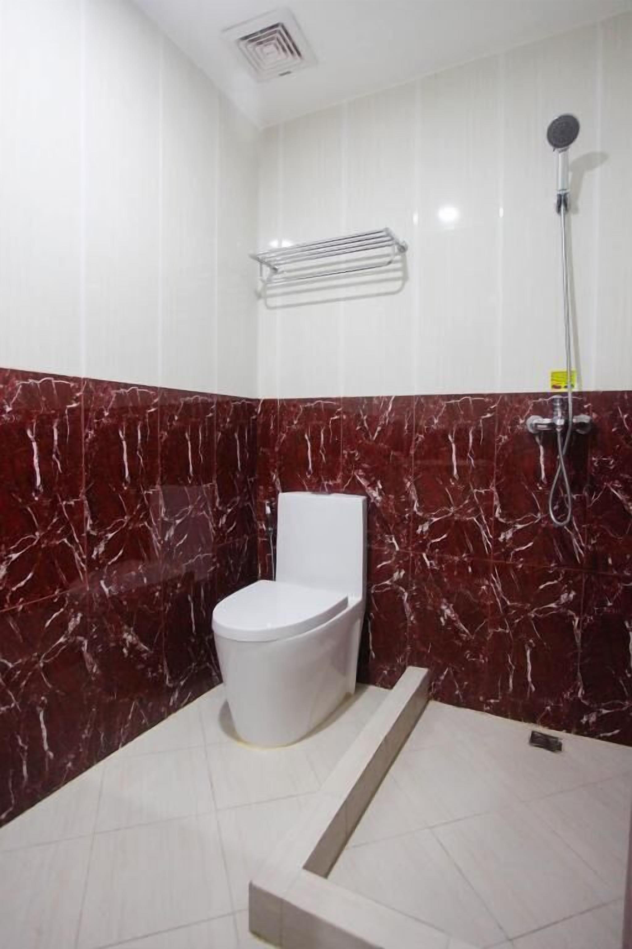 A bathroom with a white toilet, a shower, and a marble wall.
