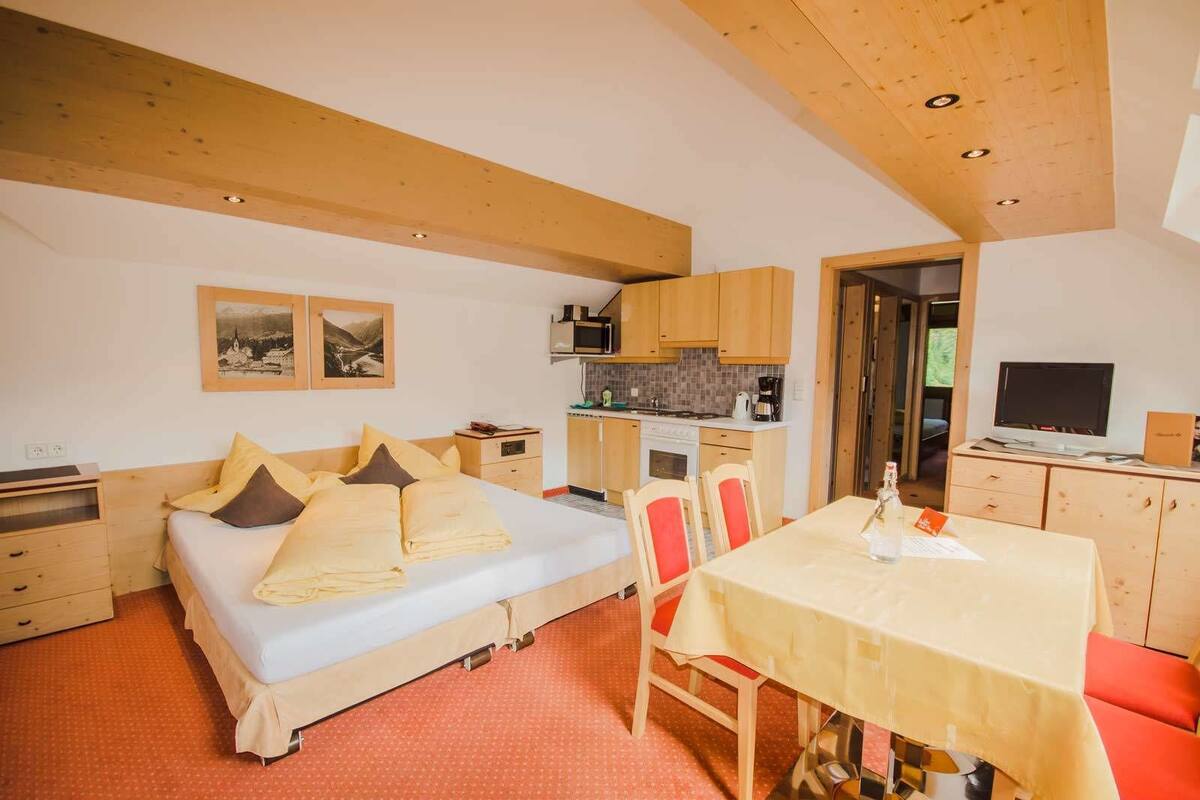 Een slaapkamer met een bed, nachtkastjes, een bureau en een stoel. Er is een kitchenette met een kookplaat, magnetron en kastjes. Een televisie staat op een standaard in de hoek.