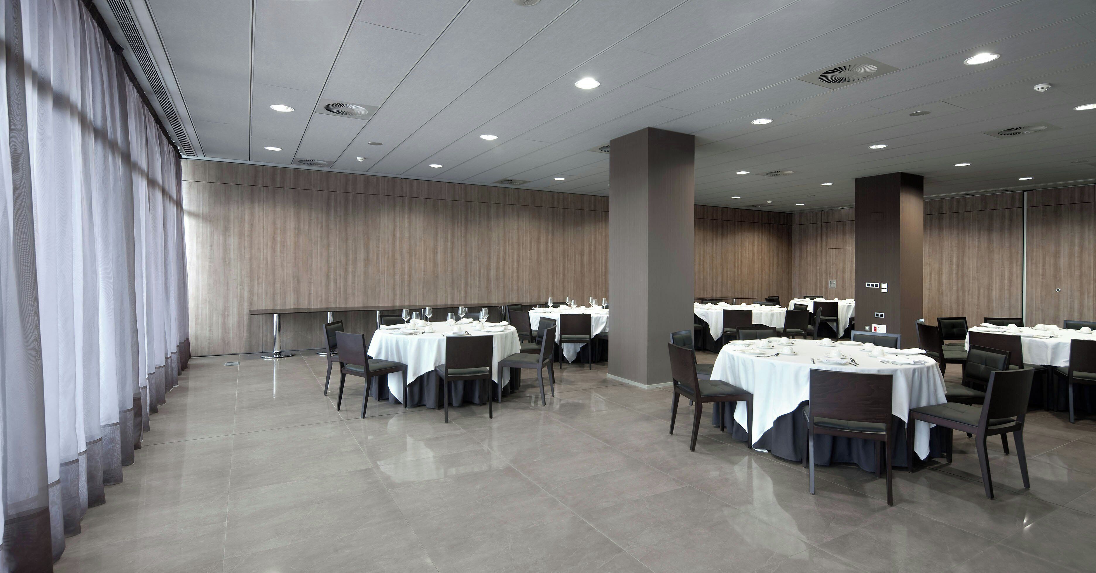 Un amplio salón de banquetes con varias mesas redondas, sillas y un techo alto con iluminación empotrada.