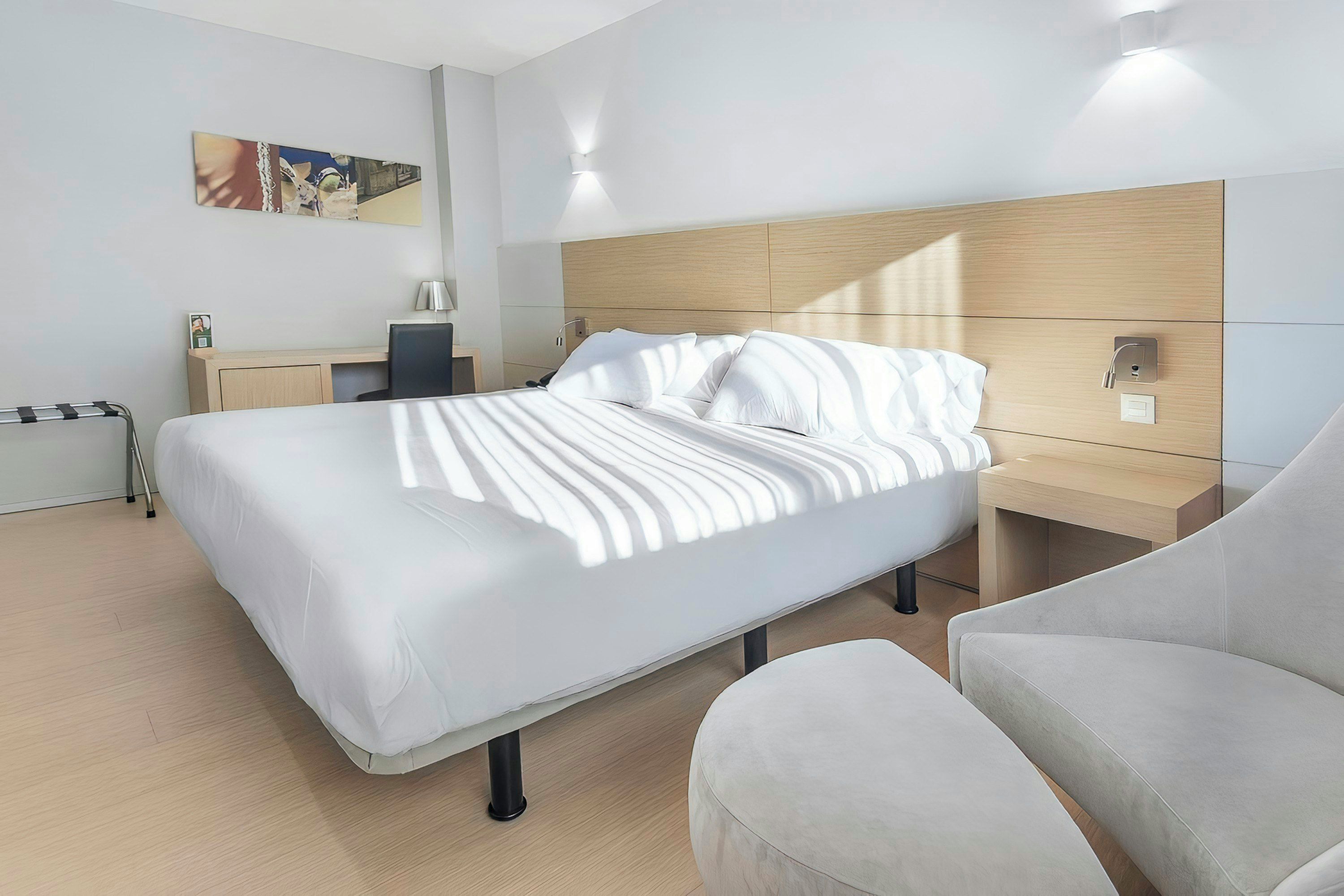 Een moderne hotelkamer met een bed, nachtkastje, lamp en een stoel.