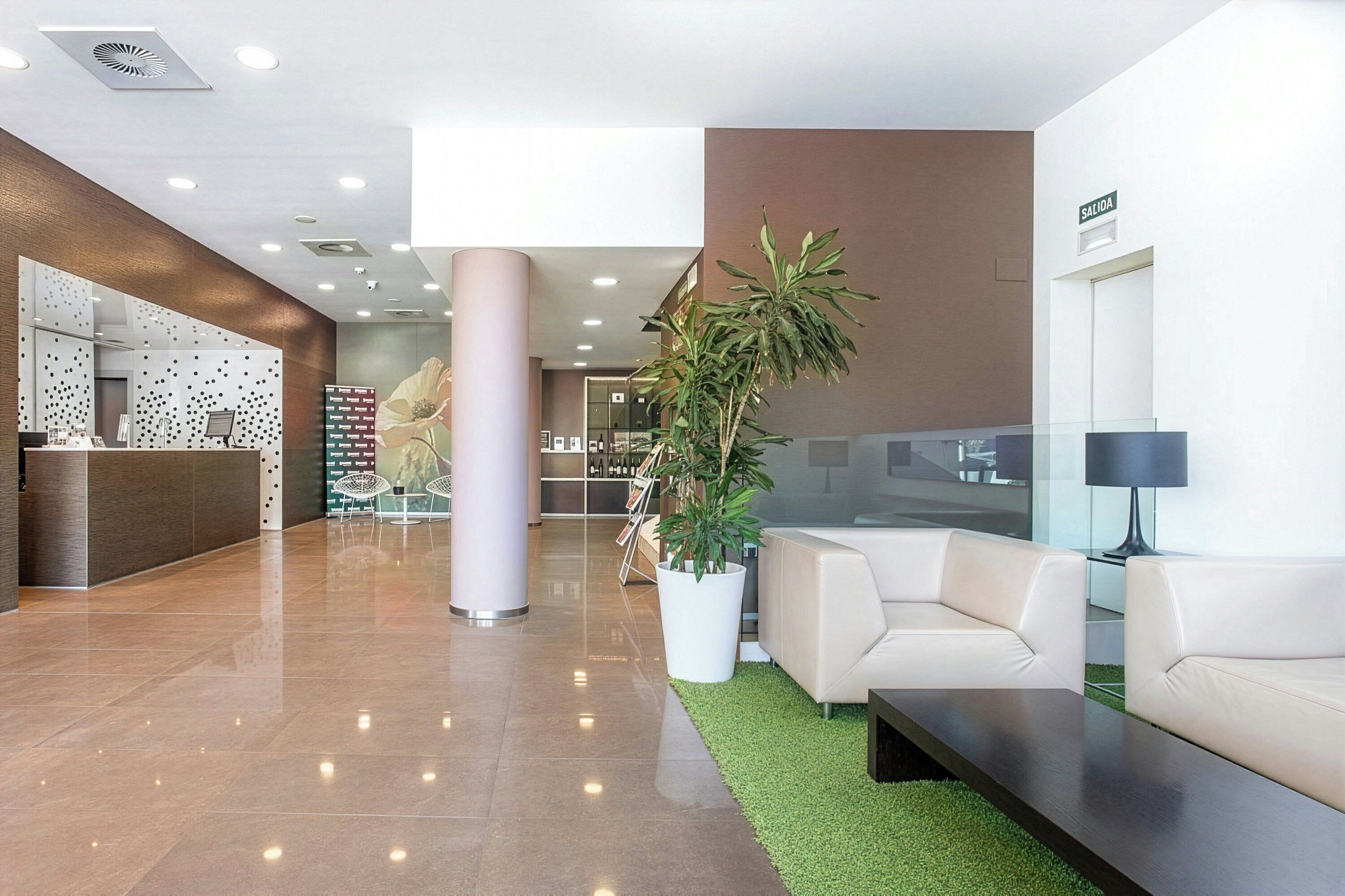 Un vestíbulo moderno con mostrador de recepción, zona de estar y una planta grande en maceta.
