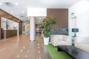 Un vestíbulo moderno con mostrador de recepción, zona de estar y una planta grande en maceta.