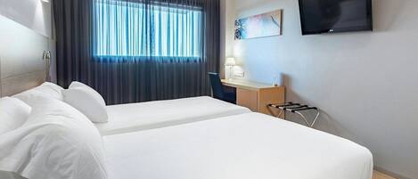 Habitación de hotel con cama, escritorio, silla, televisor y ventana con cortinas.