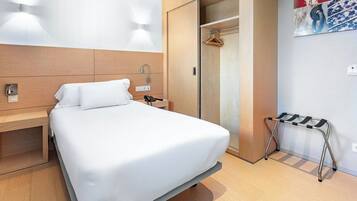 Une chambre d’hôtel comprenant un lit, une table de chevet, une lampe fixée au mur et un porte-manteau.
