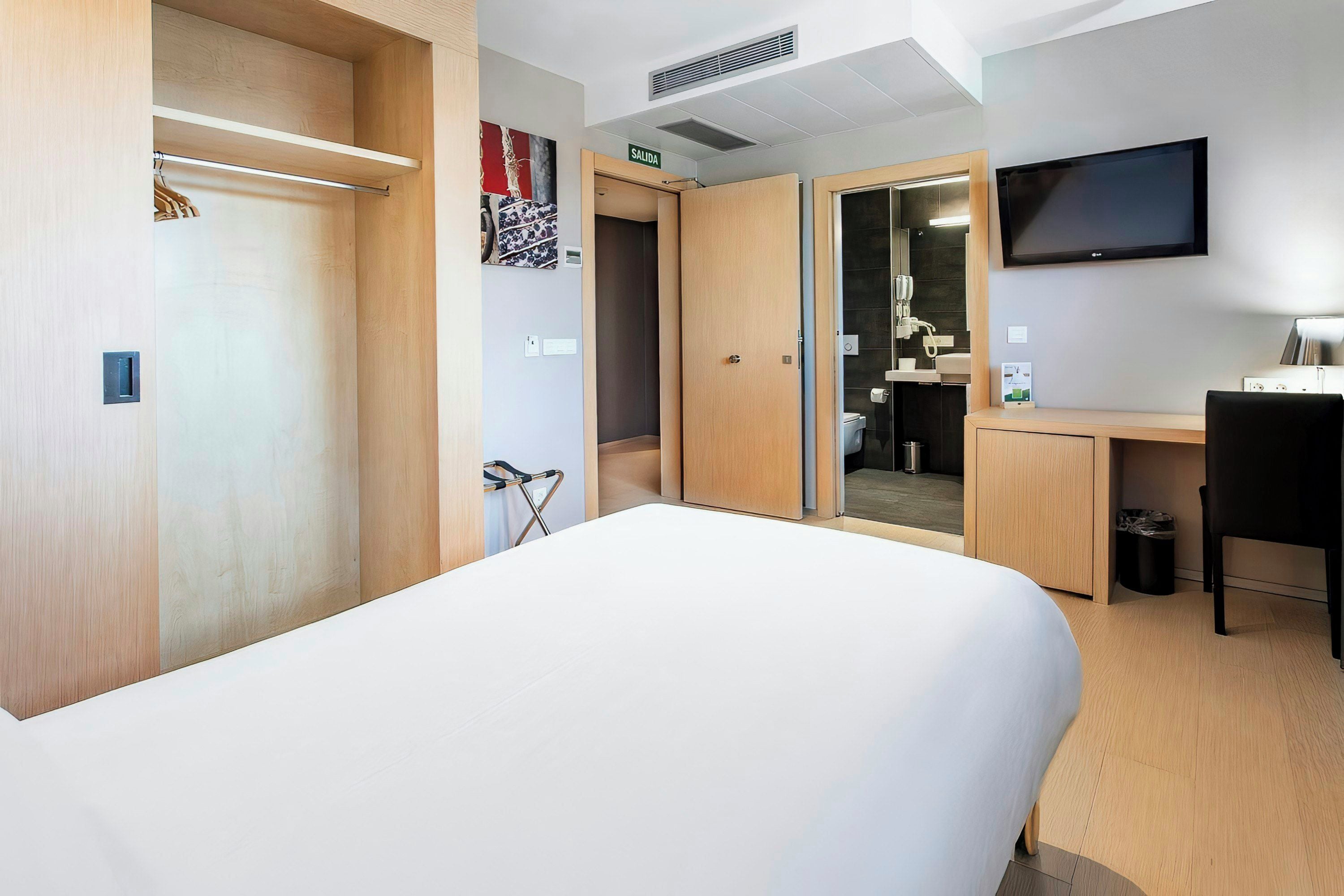 Ein Hotelzimmer mit Bett, Schreibtisch, Stuhl, Fernseher und einem durch eine offene Tür einsehbaren Badezimmer.