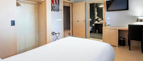 Ein Hotelzimmer mit Bett, Schreibtisch, Stuhl, Fernseher und einem durch eine offene Tür einsehbaren Badezimmer.